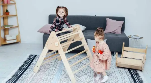 Two toddlers engage in Montessori activities for babies, climbing a wooden Pikler triangle and playing with toys in a bright, cozy room.