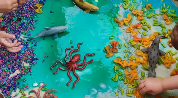 Ocean-themed sensory bin with toy sea creatures, colorful pebbles, and pasta provides engaging sensory activities for 1 year olds.