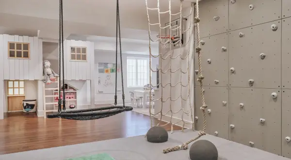 A child's indoor adventure zone with a climbing wall, net, and swing, embodying a Montessori aesthetic.