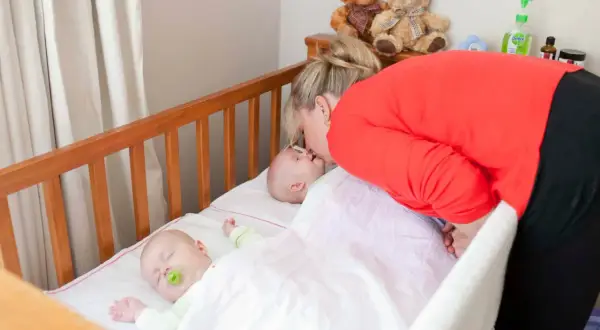 A mother kisses her baby in one of two **double baby cribs**. Another baby sleeps peacefully nearby.