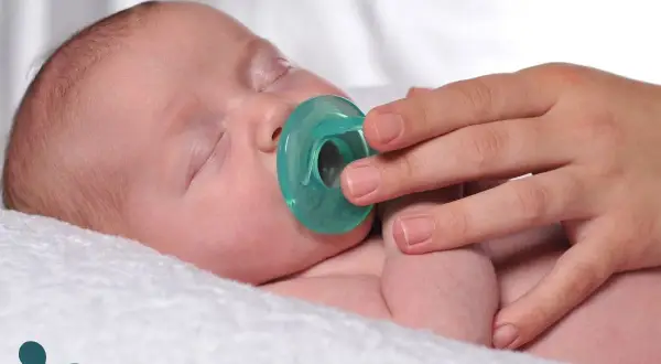 A hand gently offers a pacifier to a sleeping baby. Learn when to introduce a pacifier to a breastfed baby for optimal comfort.