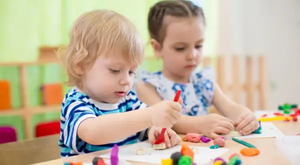 Two children engage in parallel play vs associative play, molding colorful clay at a table.