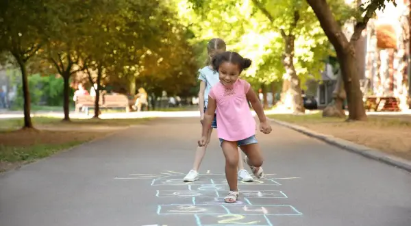 Kids learn shapes like squares and rectangles when playing hopscotch. Two girls are playing hopscotch on a sunny day.