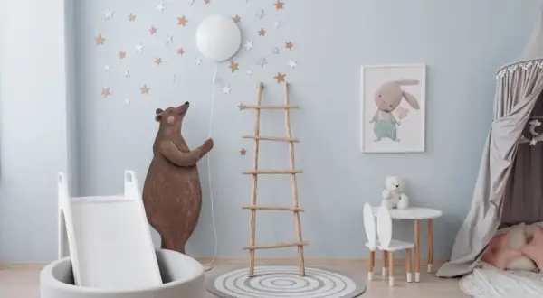 A whimsical nursery room, perfect for learning how to paint a nursery room. A bear holds a balloon, stars adorn the walls, and a bunny picture hangs above a small table.
