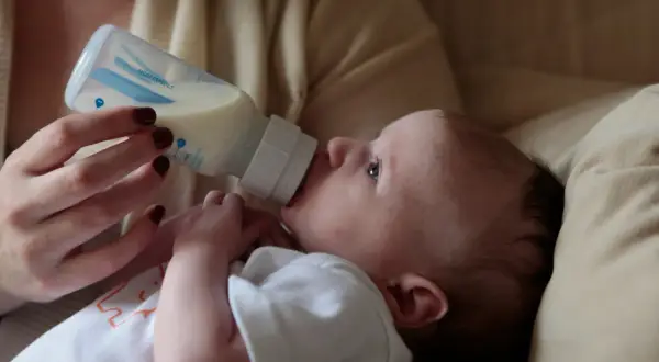 A baby drinks from a bottle. Concerns exist about does bottle feeding affect teeth alignment, but this image focuses on a moment of nourishment.
