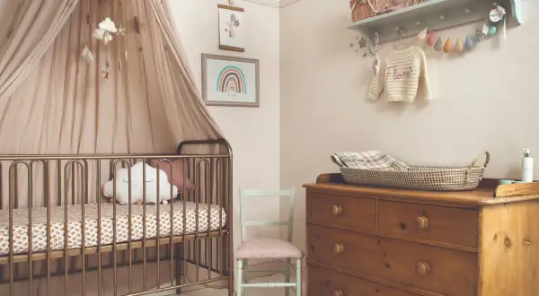 Dreamy small nursery ideas for a girl, featuring a gold crib with a cloud pillow, a rainbow print, and a vintage dresser.