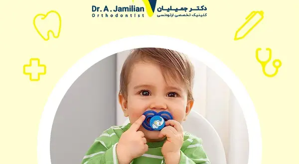A baby with a pacifier, or binky, in their mouth. The pacifier has a blue elephant design.