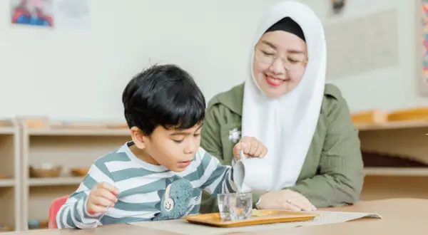 A child practices pouring water in a Montessori classroom, learning practical life skills inspired by nature.