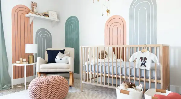 A modern nursery with rainbow wall art, a crib, and a comfy chair. Perfect for twin nursery themes with its neutral colors and playful design.