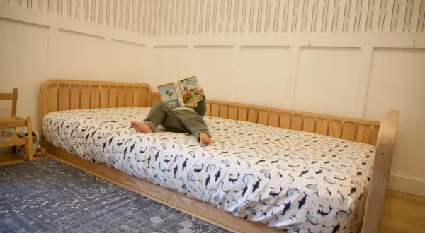 A child reads a book on a DIY Montessori bed with shark-patterned sheets.