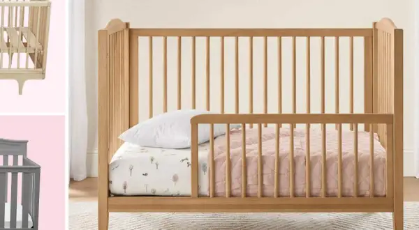 A wooden toddler bed with rails is shown, perfect for what kind of bed should a 2 year old be in. A grey crib is also visible.