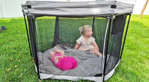 Two toddlers play in a portable playpen, a safe space often called a baby bed.