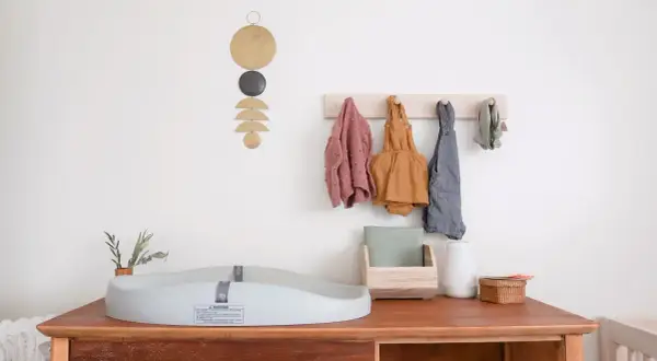 Chic corner nursery ideas: A changing pad sits on a wooden dresser with baby clothes hanging on a wall rack.