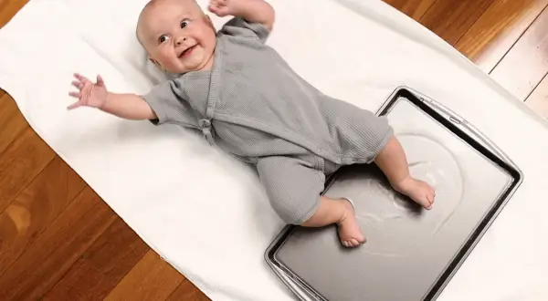 Joyful baby giggles during water play, kicking tiny feet in a shallow pan.