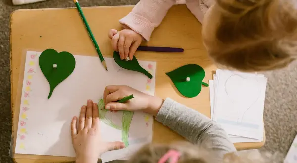 Children engage in Montessori fine motor activities, drawing and manipulating leaf shapes on a wooden table.
