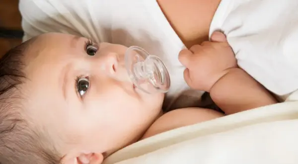 A baby with a pacifier, nestled close to their mother's chest, perhaps after breastfeeding.