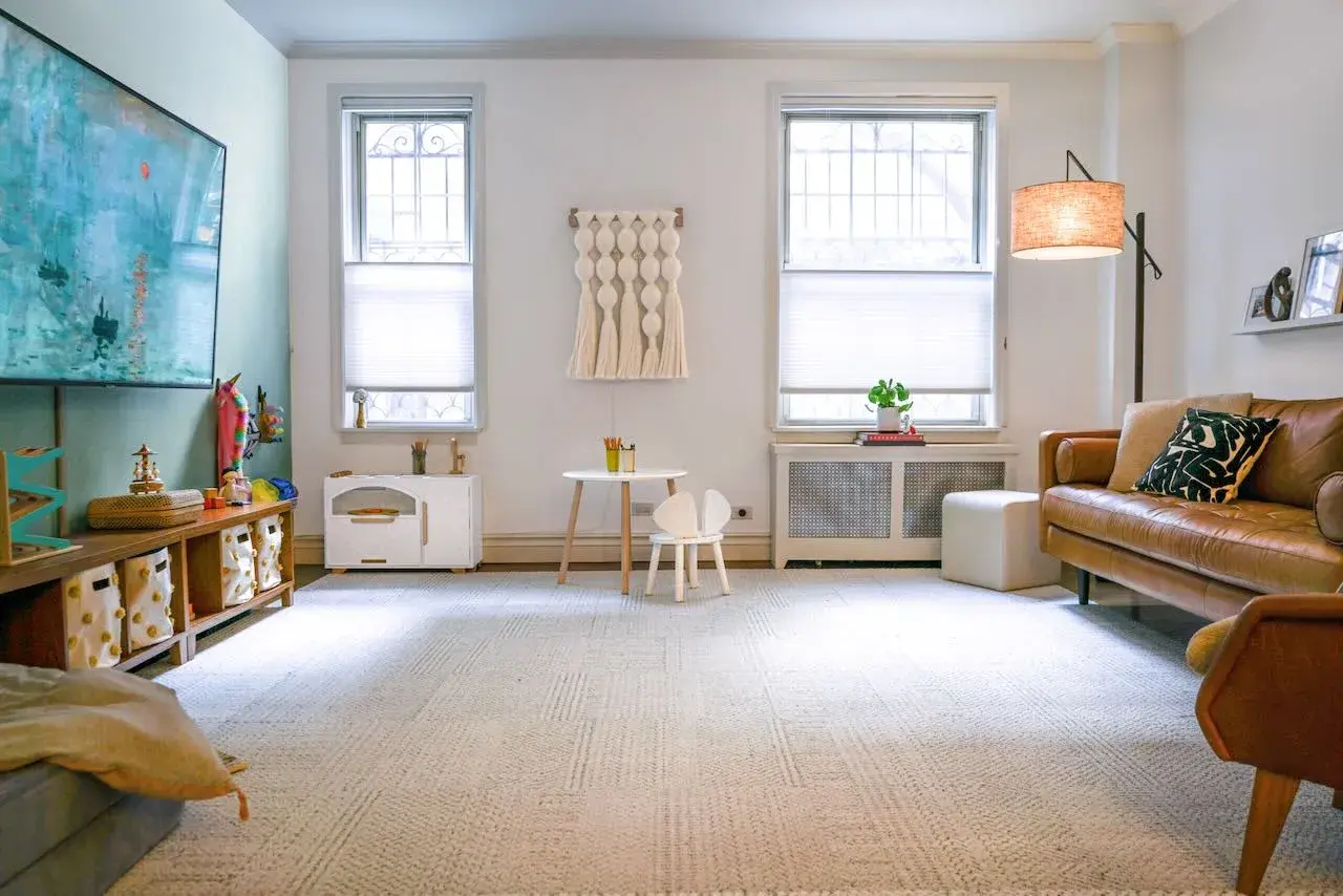 A cozy DIY play room with a brown leather sofa, a small table and chair, and toy storage.