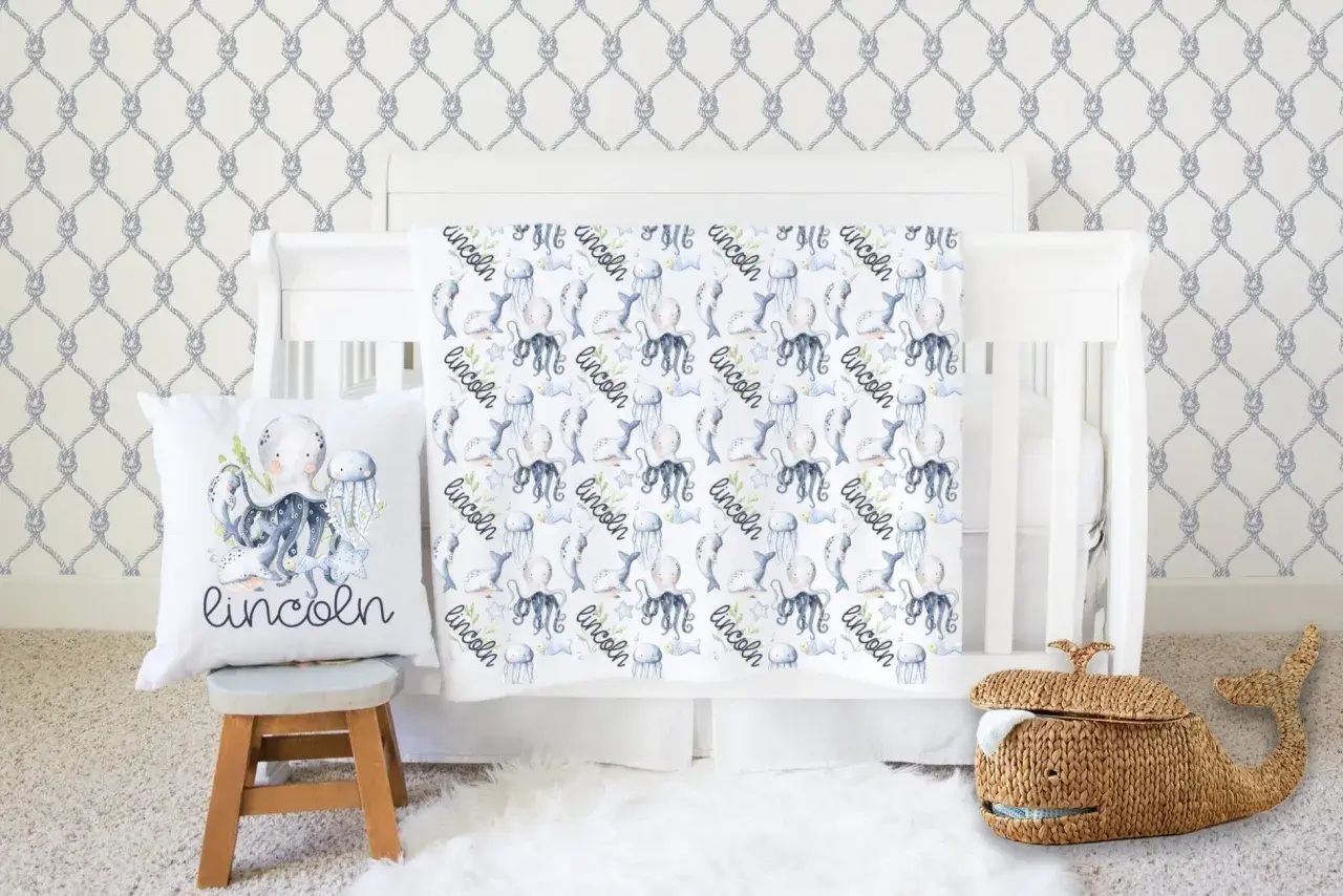 Nautical nursery with under the sea crib bedding sets featuring octopuses, narwhals, and jellyfish. A whale basket sits nearby.