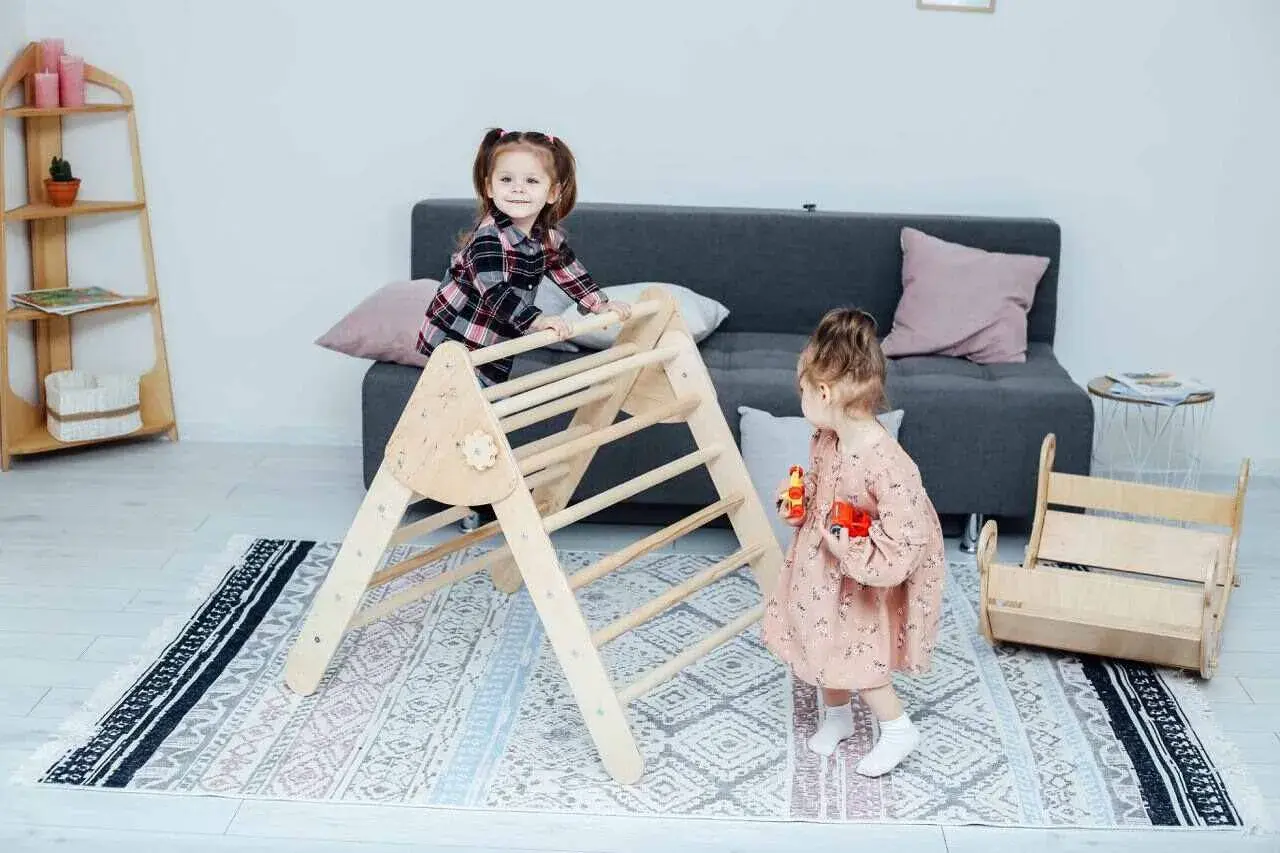Two toddlers engage in Montessori activities for babies, climbing a wooden Pikler triangle and playing with toys in a bright, cozy room.