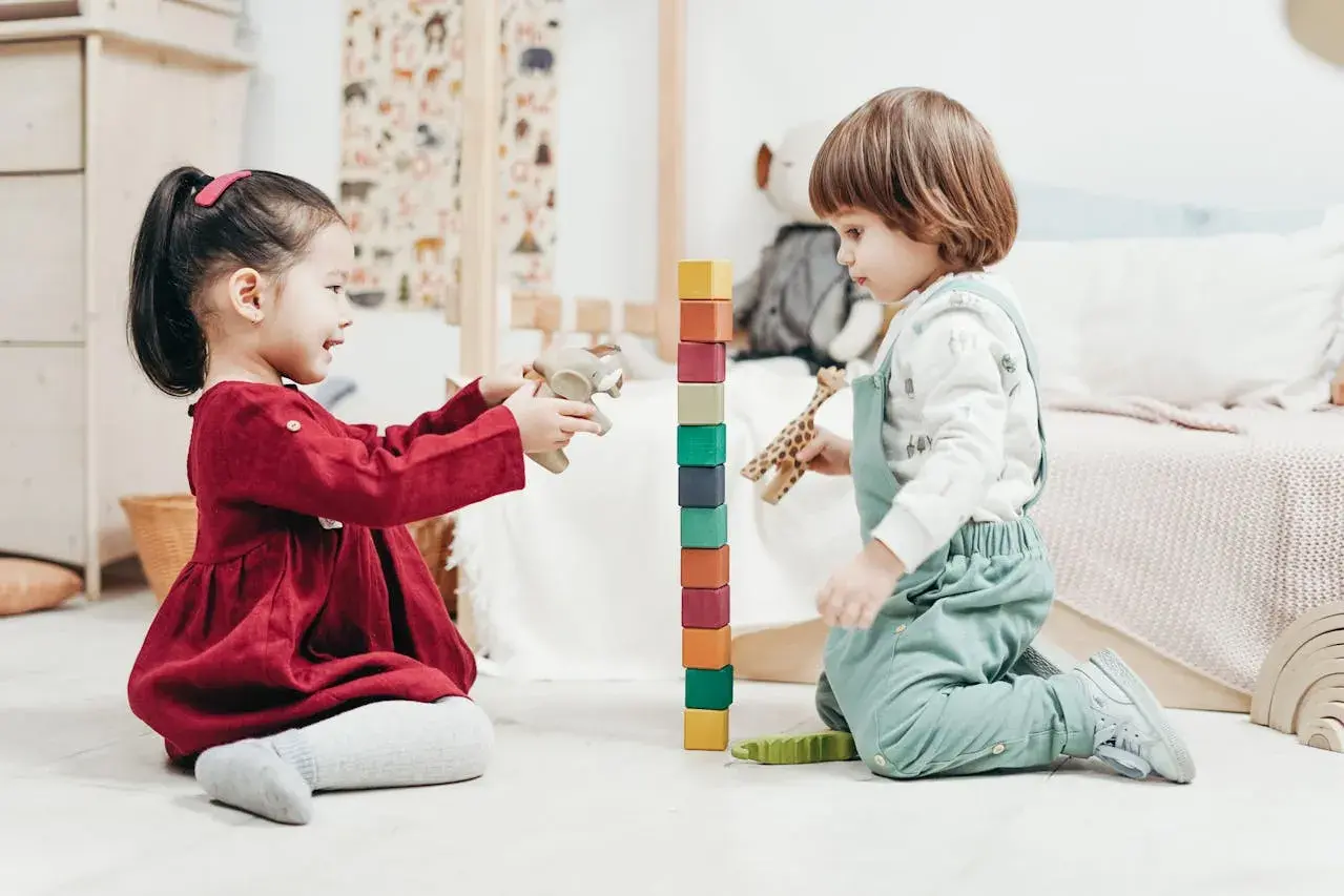 Two toddlers engage in fun games to play with one year old, stacking colorful blocks and playing with wooden animals.