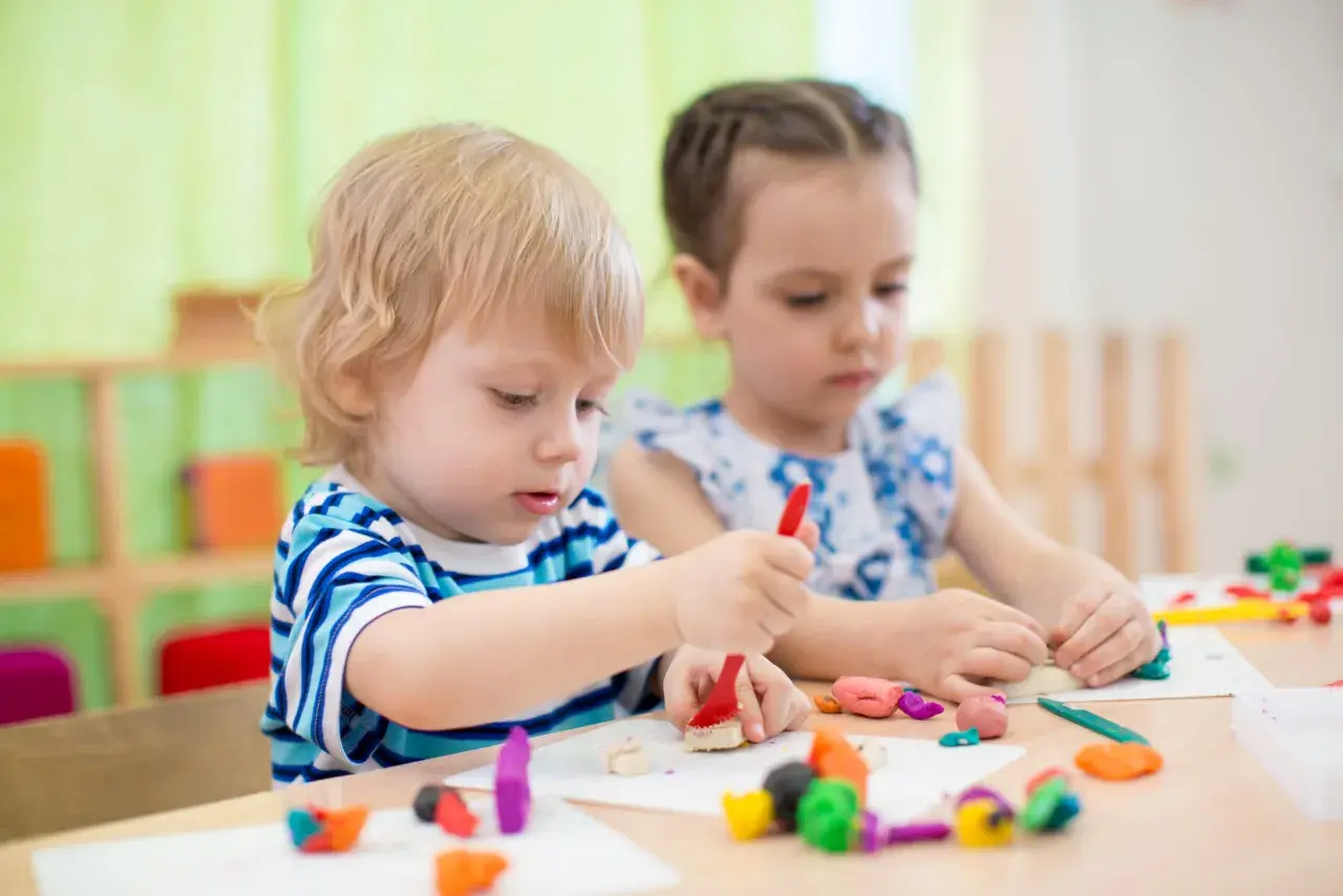 Two children engage in parallel play vs associative play, molding colorful clay at a table.