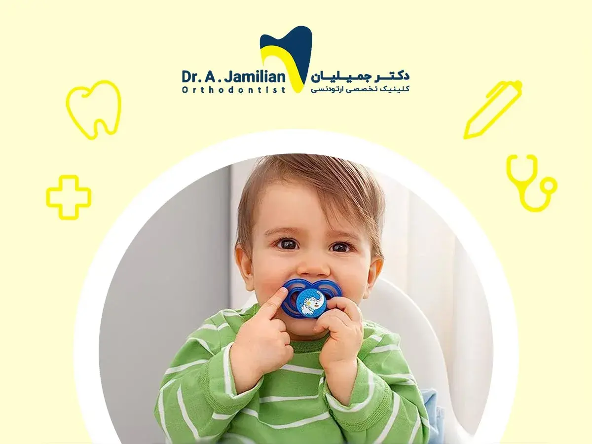 A baby with a pacifier, or binky, in their mouth. The pacifier has a blue elephant design.