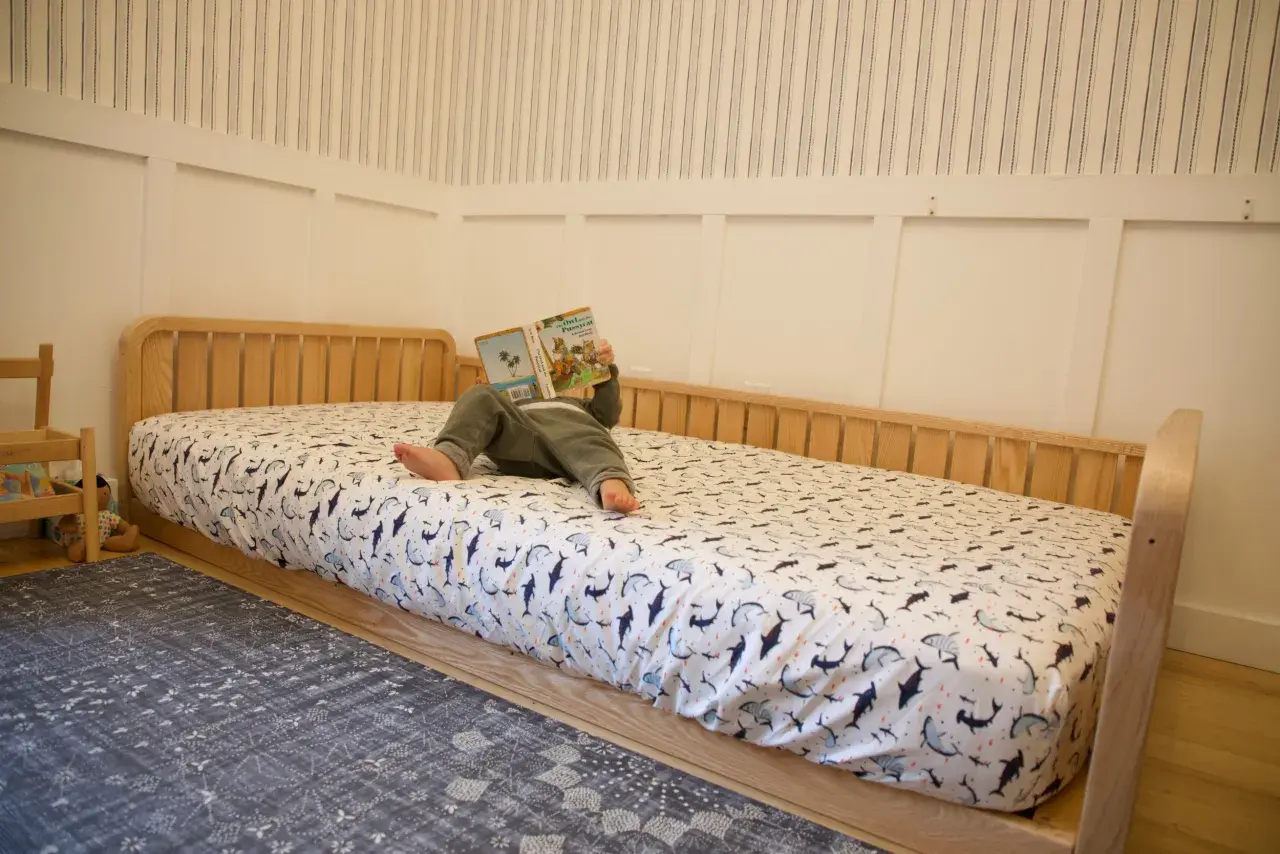 A child reads a book on a DIY Montessori bed with shark-patterned sheets.
