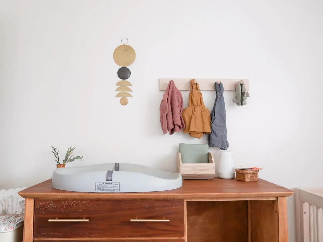 Chic corner nursery ideas: A changing pad sits on a wooden dresser with baby clothes hanging on a wall rack.