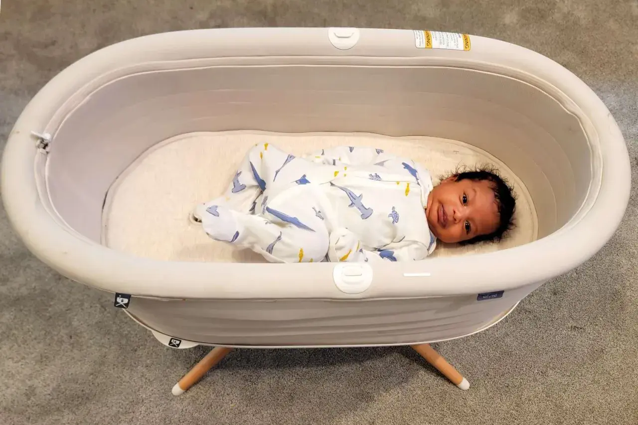 A baby sleeps soundly in a bassinet, a cozy bed for newborns. This bassinet is used for a safe and comfortable sleeping space for infants.