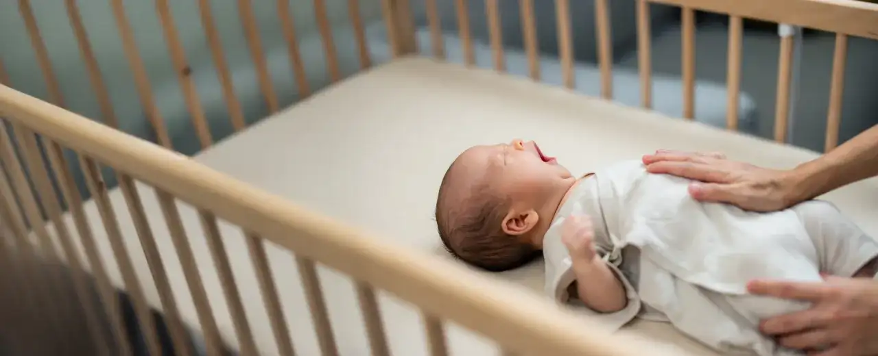 A baby yawns in a wooden crib. This image reassures parents that mini cribs are safe for their little ones.