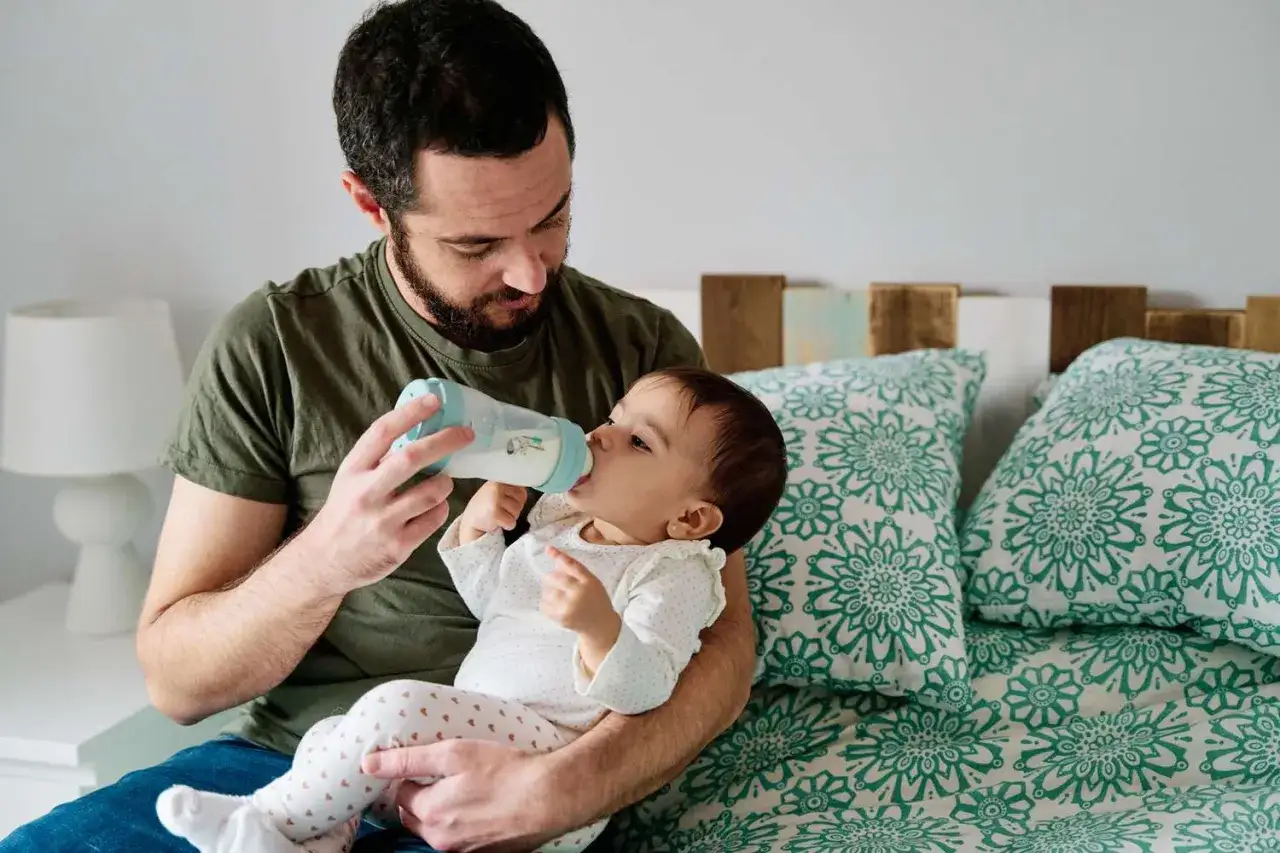 A father lovingly feeds his baby formula from a bottle, showcasing the flexibility and bonding positives of formula feeding.