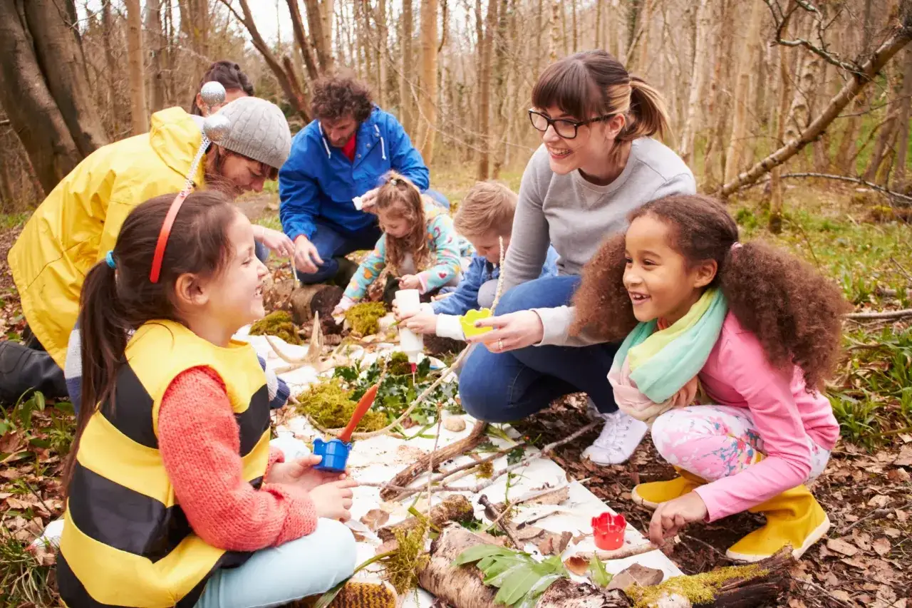 Children and adults engage in Montessori outdoor activities, exploring nature's treasures in a forest setting.