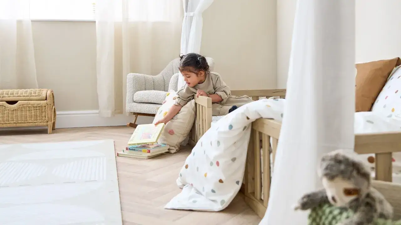 A toddler explores books in a cozy room, showcasing a peaceful Montessori for 1 year old setup with a wooden bed and soft furnishings.