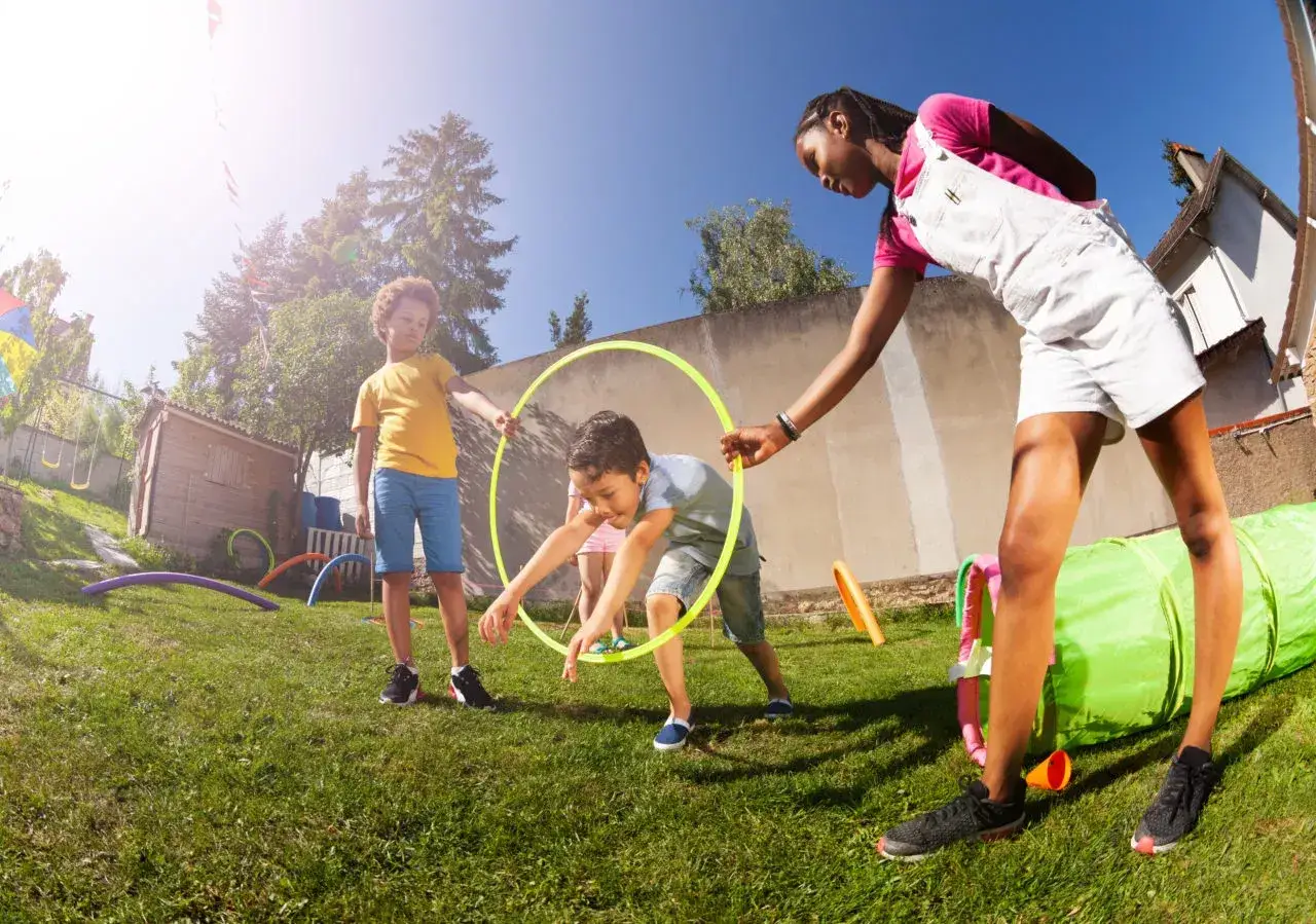 Kids enjoy gross motor activities like hula hooping and crawling through a tunnel in a sunny backyard.