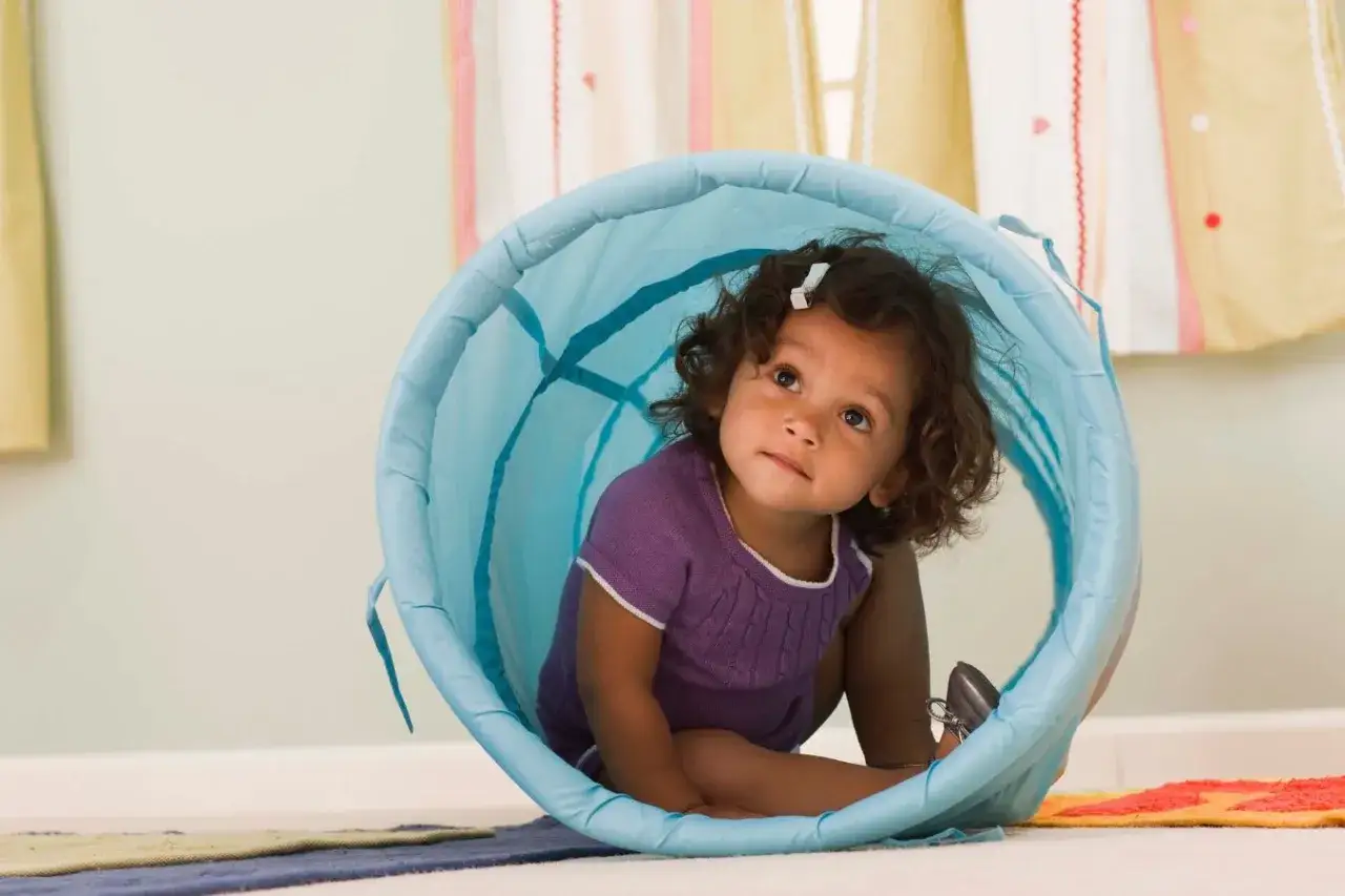 A toddler explores a blue play tunnel, engaging in gross motor activities perfect for 12-18 month olds.