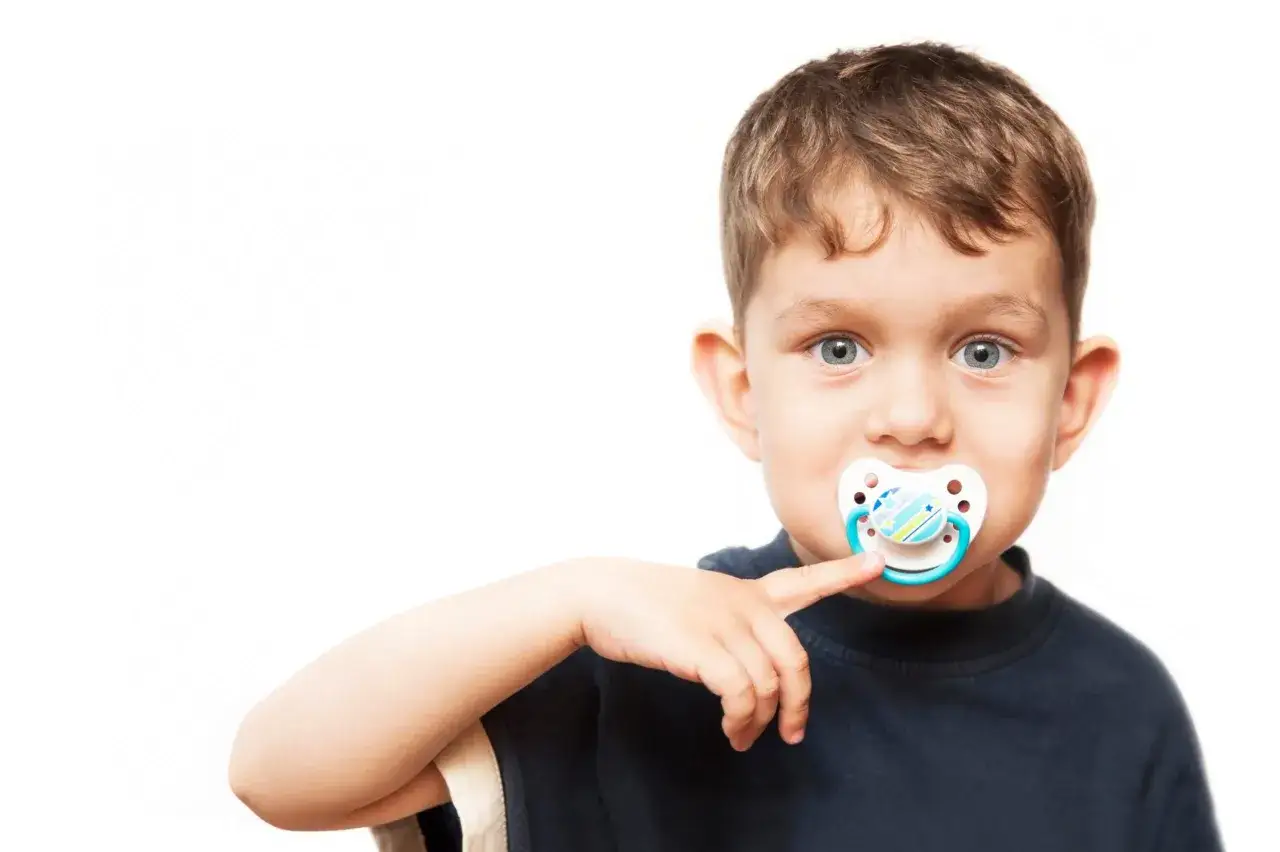 A young boy with a pacifier in his mouth, prompting the question: can a pacifier cause speech delay?