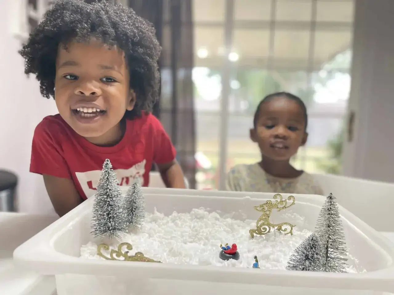 Two happy children explore a winter sensory bin filled with fluffy 