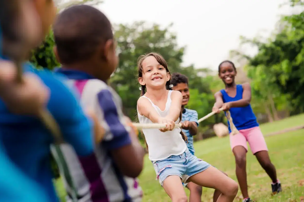 Kids enjoy tug-of-war, a fun gross motor activity for 5 year olds, pulling a rope in a park with smiles and determination.