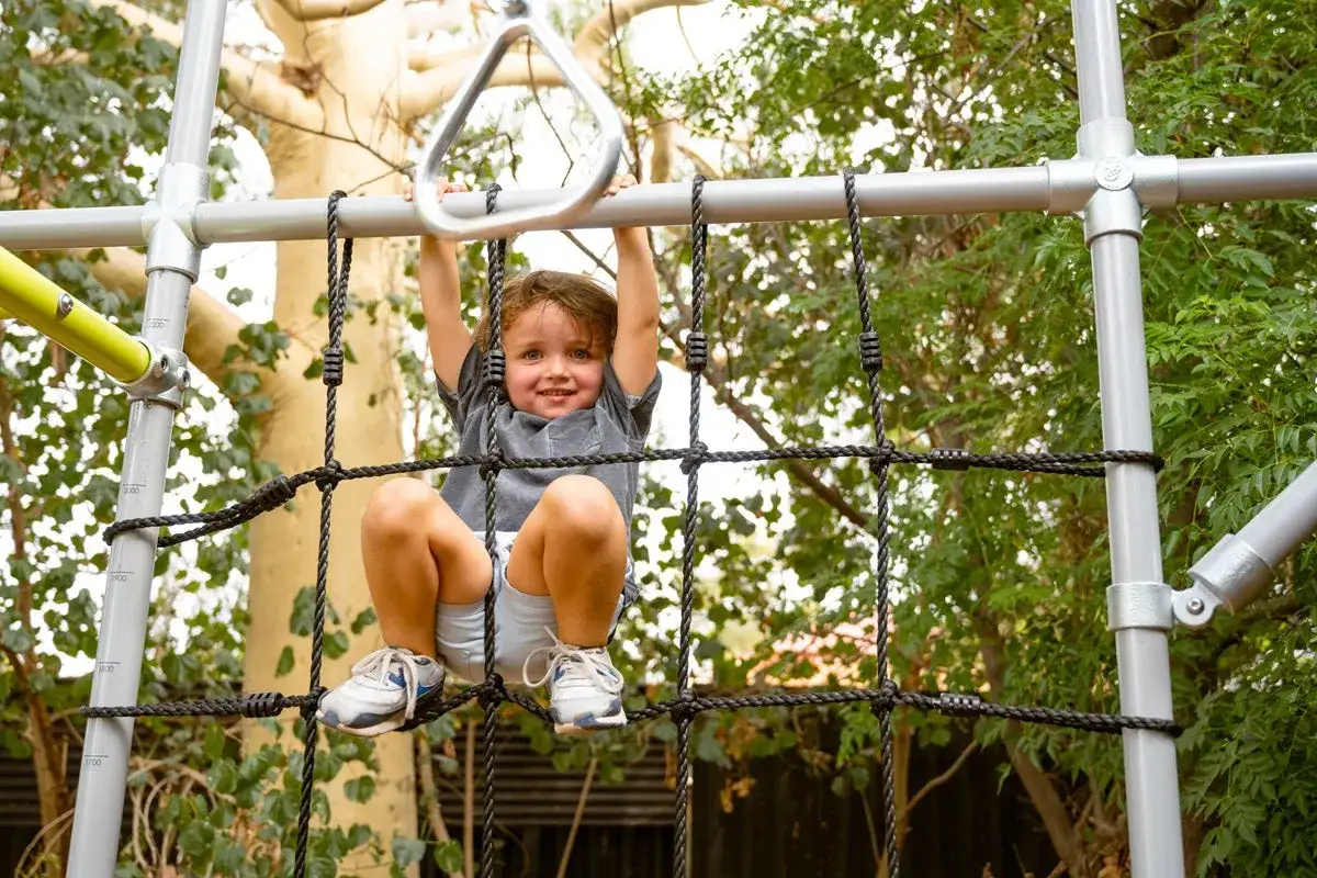 A happy toddler enjoys climbing activities on a jungle gym, reaching for a metal ring.
