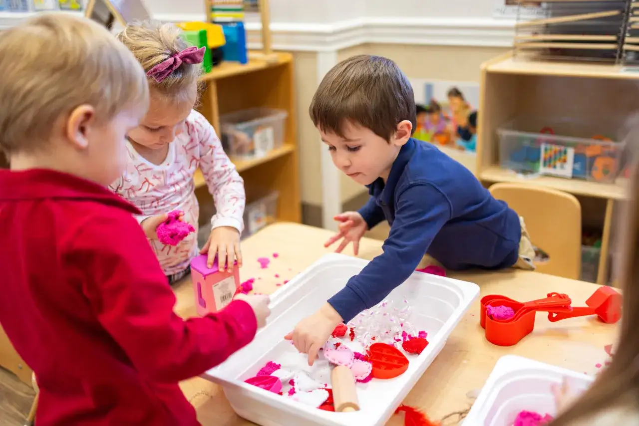 Children explore kinetic sand in a sensory bin, learning through touch and play. This shows why sensory bins are important for development.
