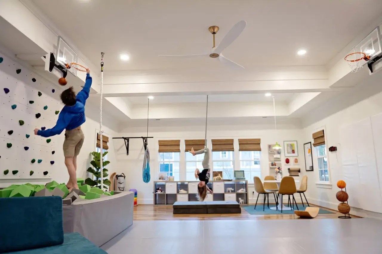 Kids enjoy the benefits of parallel play in a fun gym: one shoots hoops, another hangs upside down.