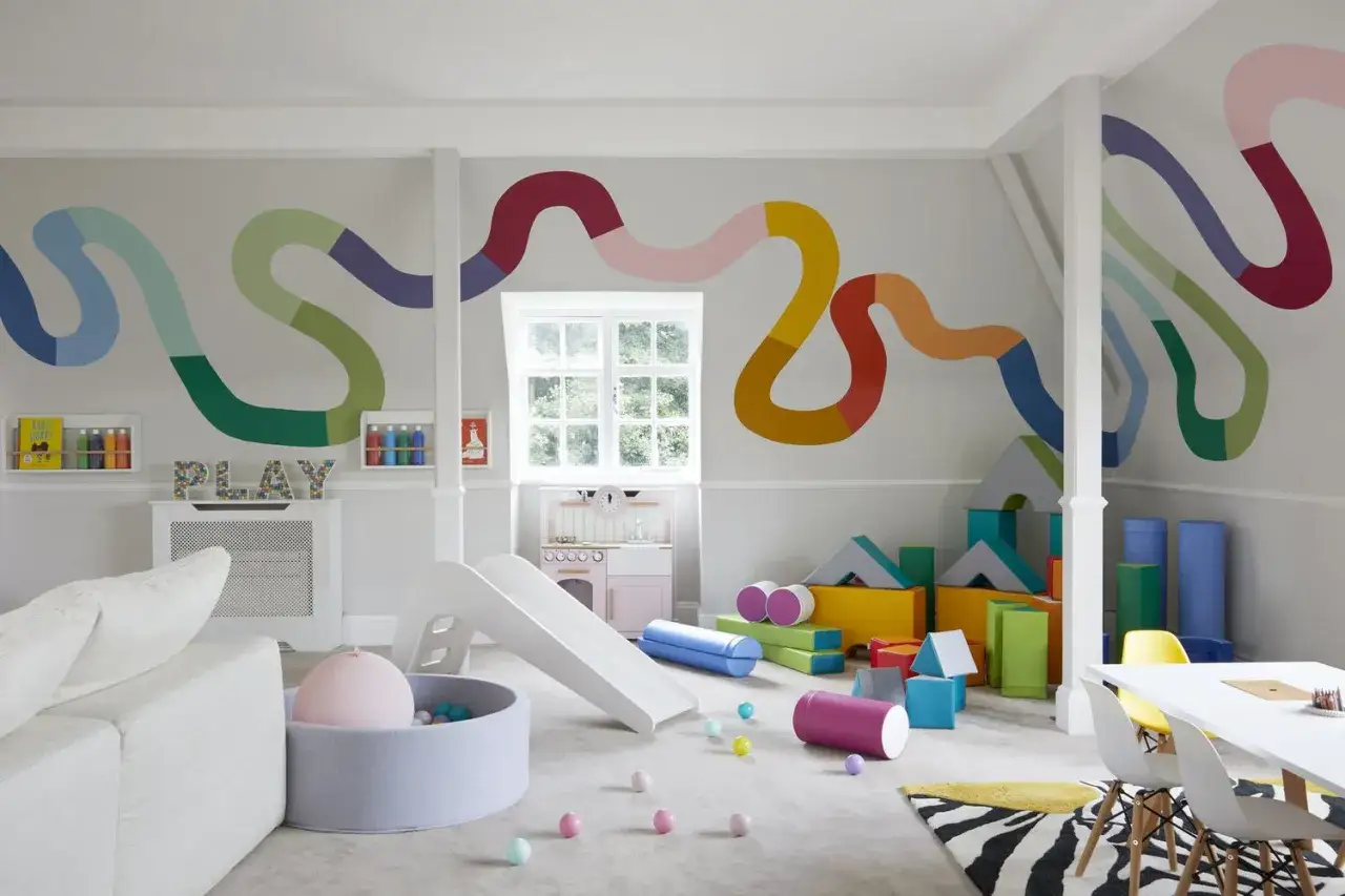 A vibrant DIY play room with a colorful wall mural, soft play area, slide, and building blocks.