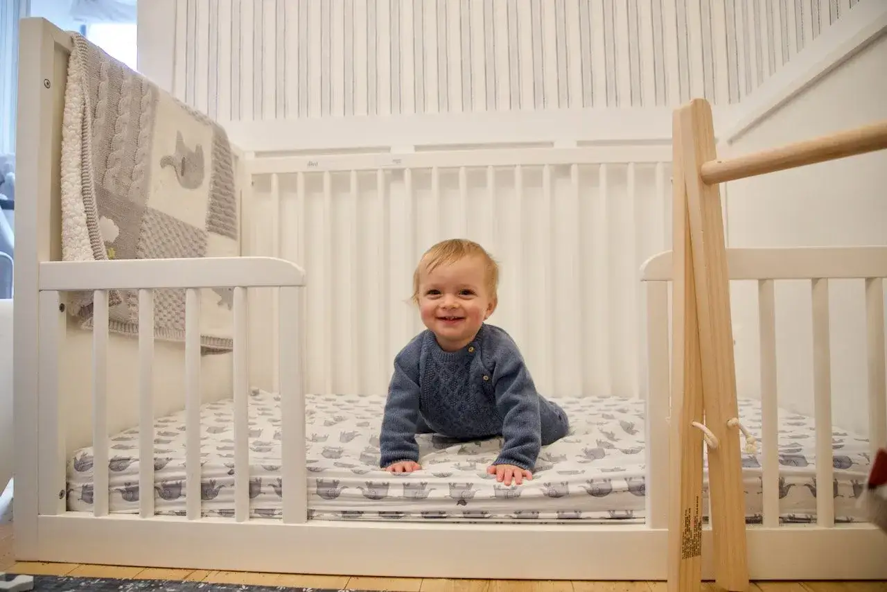 A happy baby crawls on a crib mattress, exploring their space. This crib offers a safe alternative to a floor bed for little ones.