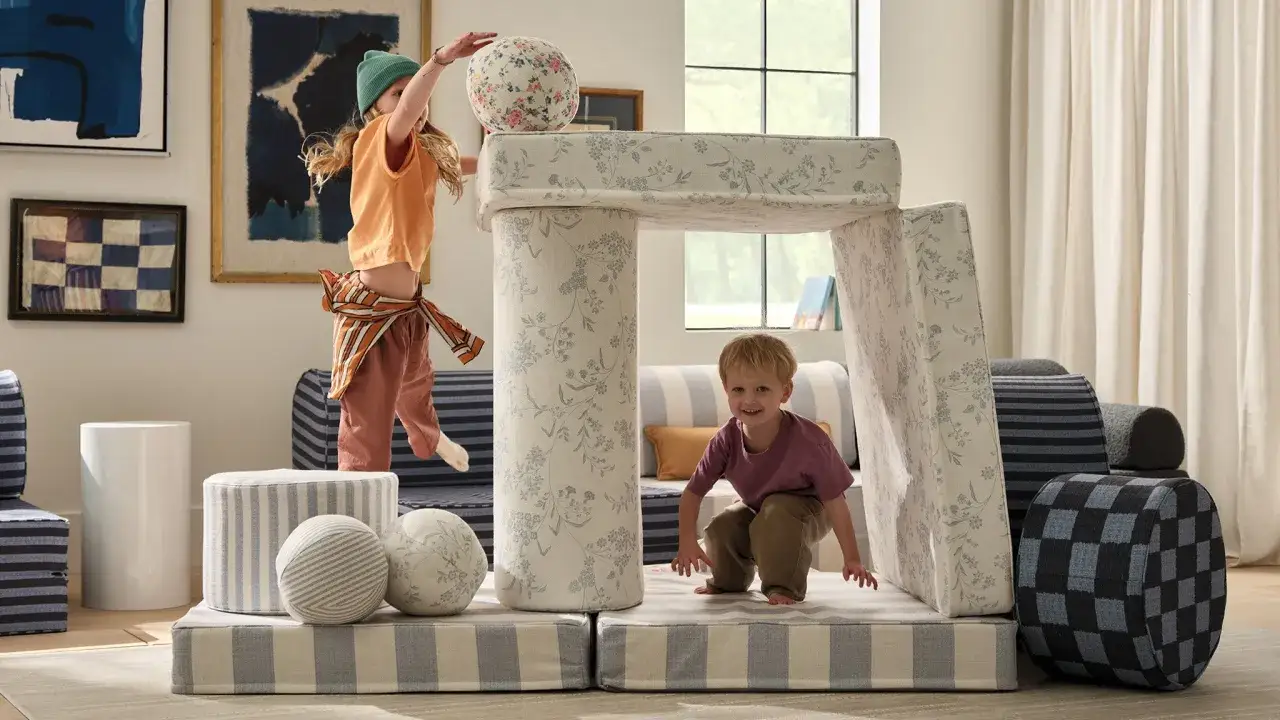 Children play in a room with Montessori organization at home, featuring soft play structures and art.