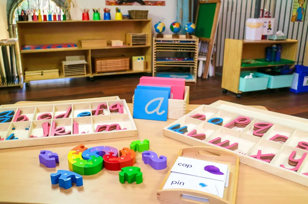 Montessori language materials, including movable alphabet letters and puzzle pieces, are laid out on a table, ready for learning.