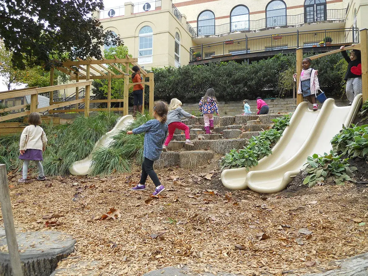Children play on slides and wooden steps in a vibrant Montessori garden.