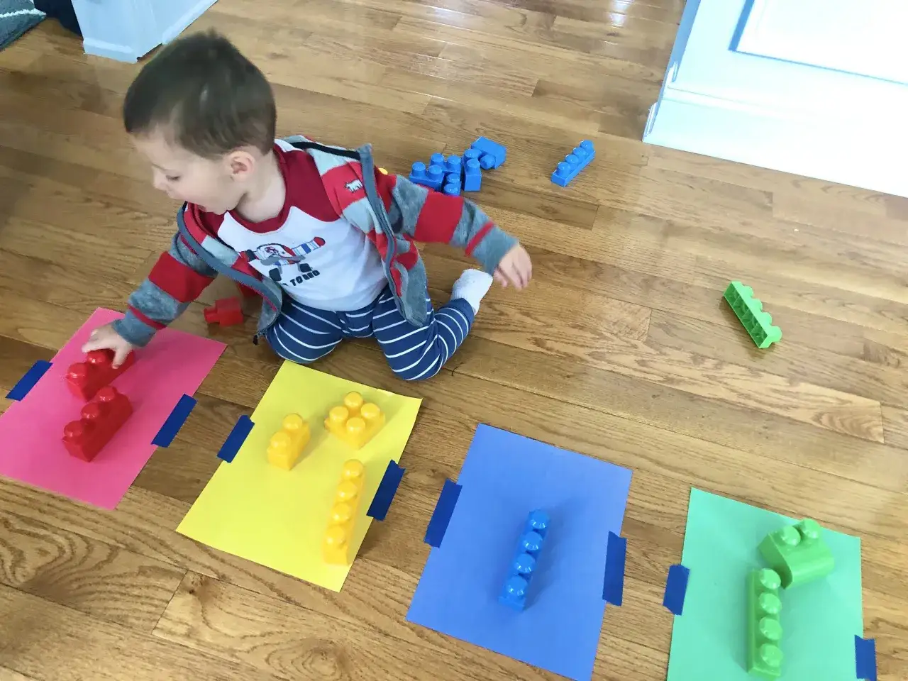 A toddler learns colors by matching red, yellow, blue, and green blocks to colored paper.
