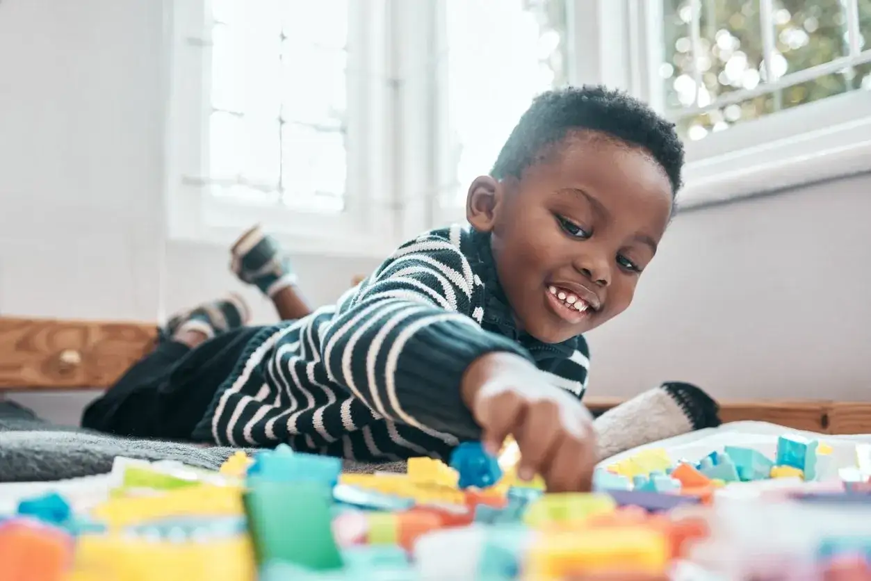 A happy toddler plays with colorful building blocks, a perfect example of what to do with toddlers at home for engaging fun and learning.