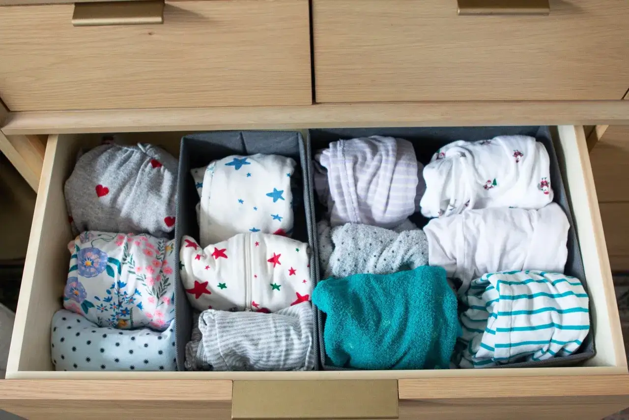 Neatly folded baby clothes in drawer dividers. This image shows how to organize baby clothes with cute patterns like hearts, stars, and flowers.