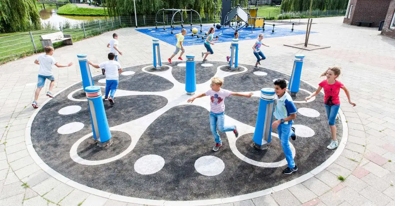Children engage in fun gross motor skills activities in school, running and jumping around a circular play structure with blue poles.